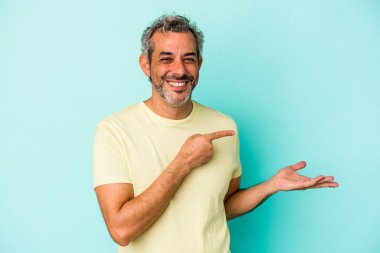 Mavi arka planda izole edilmiş orta yaşlı beyaz bir adam palmiye üzerinde bir kopya alanı tutarken heyecanlı..