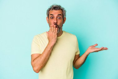 Mavi arka planda izole edilmiş orta yaşlı beyaz bir adam avuç içinin fotokopi alanından etkilenmiş..