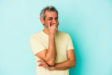 Mavi arka planda izole edilmiş orta yaşlı beyaz bir adam güler, kaygısız, doğal duygular.