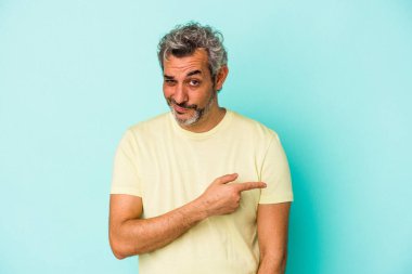Mavi arka planda izole edilmiş orta yaşlı beyaz bir adam gülümsüyor ve boş alanda bir şeyler gösteriyor..