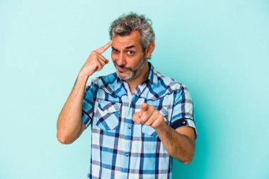 Mavi arka planda izole edilmiş orta yaşlı beyaz bir adam şakağı parmağıyla işaret ediyor, düşünüyor ve bir göreve odaklanıyor..