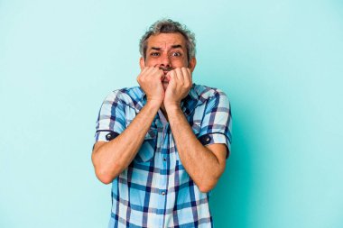 Mavi arka planda izole edilmiş, tırnak yiyen, gergin ve endişeli orta yaşlı bir beyaz adam..