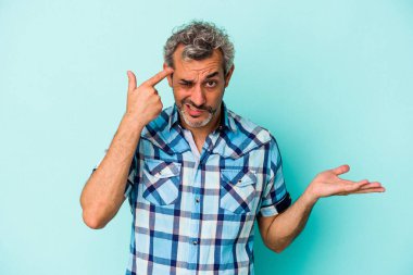 Mavi arka planda izole edilmiş orta yaşlı beyaz bir adam işaret parmağıyla hayal kırıklığı jesti yapıyor..