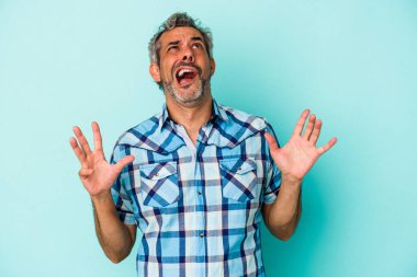 Mavi arka planda izole edilmiş orta yaşlı beyaz bir adam gökyüzüne haykırıyor, yukarı bakıyor, hayal kırıklığına uğramış..
