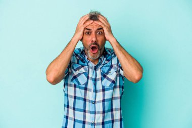 Mavi arka planda izole edilmiş orta yaşlı beyaz adam şaşırdı ve şok oldu..