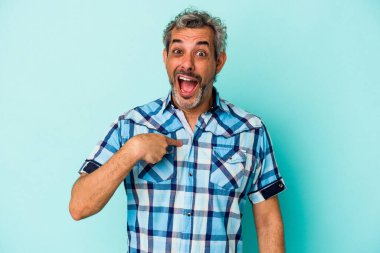 Mavi arka planda izole edilmiş orta yaşlı beyaz bir adam parmağını göstererek şaşırdı, geniş bir gülümsemeyle..