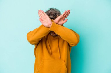 Mavi arka planda izole edilmiş orta yaşlı beyaz bir adam iki kolu çapraz tutuyor, inkar kavramı.