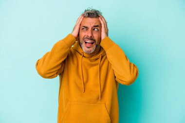 Orta yaşlı, beyaz bir adam mavi arka planda izole edilmiş kulakları kulaklarıyla kapatıyor ve çok fazla ses duymamaya çalışıyor..