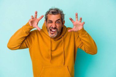 Mavi arka planda izole edilmiş orta yaşlı beyaz adam pençelerini kedi taklidi yaparken gösteriyor, agresif bir hareket..