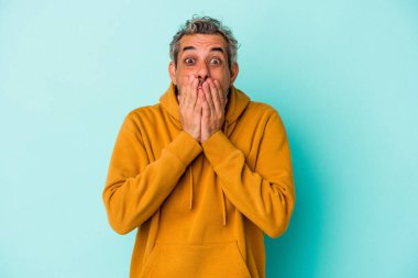 Mavi arka planda izole edilmiş orta yaşlı beyaz adam şok olmuş, ağzı ellerle kaplanmış, yeni bir şey keşfetmeye hevesli..