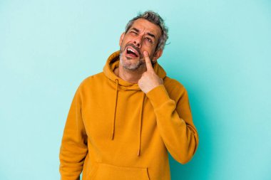 Orta yaşlı beyaz bir adam mavi arka planda izole edilmiş, ağlıyor, bir şeyden mutsuz, acı ve kafa karışıklığı konsepti..