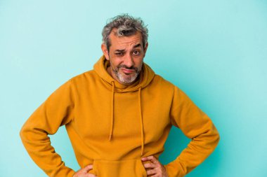 Mavi arka planda izole edilmiş orta yaşlı beyaz bir adam üzgün, ciddi bir yüz, sefil ve hoşnutsuz hissediyor..