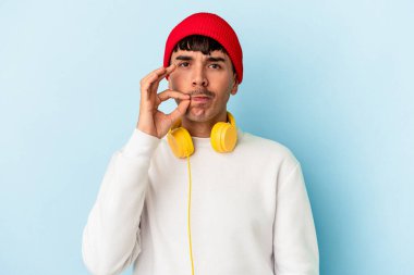 Genç melez adam mavi arka planda izole edilmiş müzik dinliyor parmakları dudaklarında bir sır saklıyor.