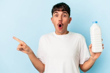 Mavi arka planda bir şişe süt tutan melez genç adam yan tarafı işaret ediyor.