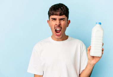 Genç melez adam mavi arka planda izole edilmiş bir şişe süt tutuyor. Çok sinirli ve agresif bağırıyor..