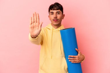 Genç melez bir adam pembe arka planda izole edilmiş bir spor paspası tutuyor..