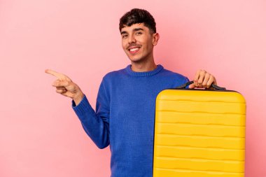 Genç melez adam pembe arka planda tek başına seyahat edecek gülümseyecek ve boş alanda bir şeyler gösterecek..