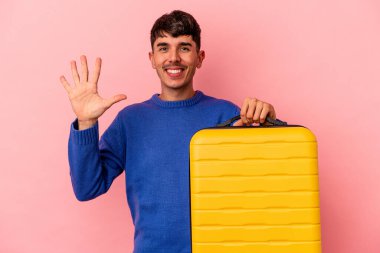 Genç melez adam pembe arka planda tek başına seyahat edecek gülümseyerek beş numarayı parmaklarıyla gösterecek..