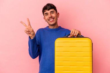 Genç melez adam pembe arka planda yalnız seyahat edecek neşeli ve kaygısız parmaklarıyla barış sembolü gösterecek..