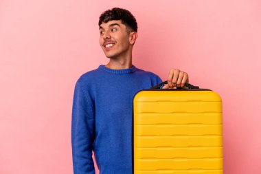Genç melez adam pembe arka planda tek başına seyahat edecek. Gülümsüyor, neşeli ve keyifli görünüyor..