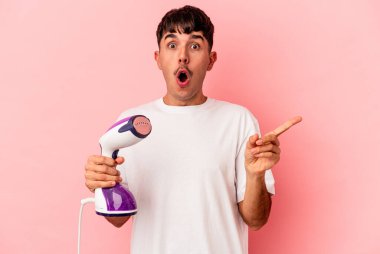 Pembe arka planda demir tutan melez genç bir adam yan tarafı işaret ediyor.