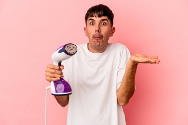 Pembe arka planda izole edilmiş demir tutan genç bir ırk omuz silker ve gözleri açık kalır..