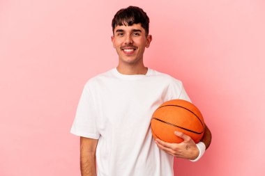Basketbol oynayan genç melez adam pembe arka planda izole edilmiş mutlu, güler yüzlü ve neşeli..