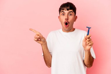 Genç melez adam elinde jilet tutuyor. Pembe arka planda izole edilmiş. Yan tarafı gösteriyor.