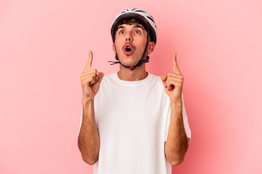 Pembe arka planda izole edilmiş kask takan genç melez bir adam ağzı açık bir şekilde üst tarafı işaret ediyor..