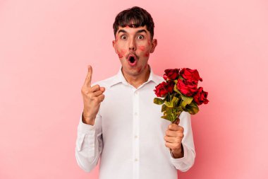 Genç melez bir adam pembe arka planda izole edilmiş bir buket çiçek tutuyor. Harika bir fikri var, yaratıcılık kavramı..