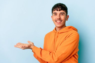 Genç melez adam mavi arka planda izole edilmiş bir şekilde avucunun içinde bir kopya alanı tutuyor..