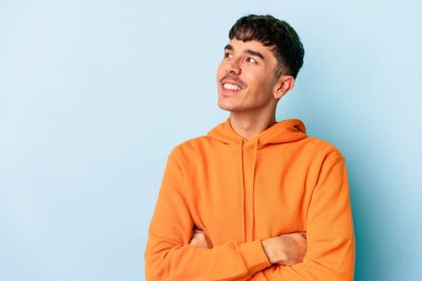 Mavi arka planda soyutlanmış genç melez adam kollarını kavuşturarak gülümsüyor..