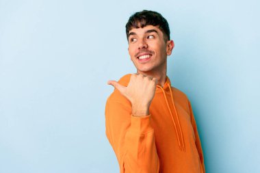 Genç melez adam mavi arka planda izole edilmiş, başparmak uzakta, gülüyor ve kaygısız..