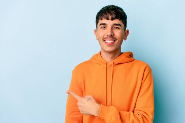 Genç melez adam mavi arka planda izole edilmiş gülümseyen ve işaret eden boş alanda bir şey gösteriyor..