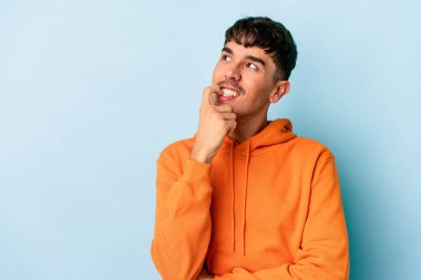 Genç melez adam mavi arka planda izole edilmiş rahat bir şekilde fotokopi odasına bakan bir şeyi düşünüyor..