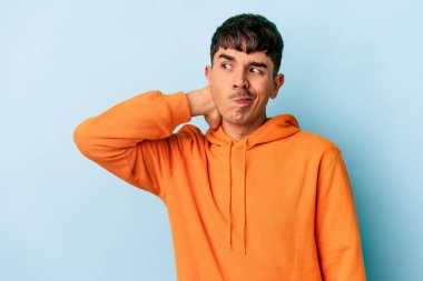 Genç melez adam mavi arka planda izole edilmiş kafasının arkasına dokunuyor, düşünüyor ve bir seçim yapıyor..