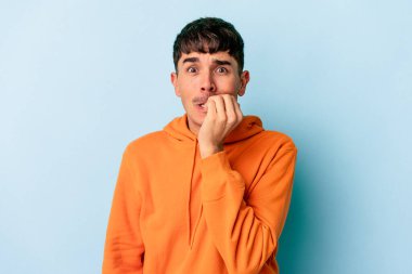 Genç melez adam mavi arka planda izole edilmiş tırnak yiyor, gergin ve çok endişeli..