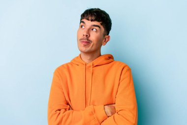 Genç melez adam mavi arka planda izole edilmiş hedeflerine ve amaçlarına ulaşma hayali kuruyor.