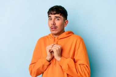 Genç melez adam mavi arka planda izole edilmiş korkmuş ve korkmuş..