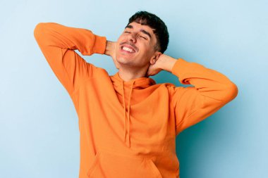 Genç melez adam mavi arka planda izole edilmiş, kollarını uzatmış, rahat bir konumda..