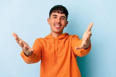 Mavi arka planda izole edilmiş genç melez bir adam hoş bir yüz ifadesi sergiliyor..