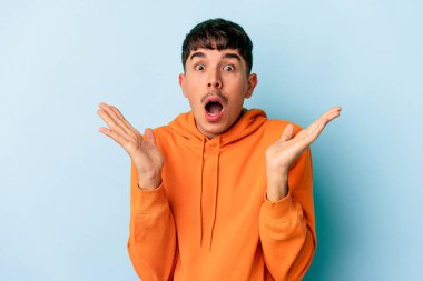 Genç melez adam mavi arka planda izole edildi. Şaşırdı ve şok oldu..