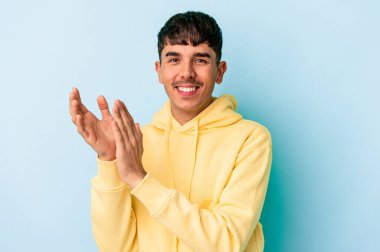 Genç melez adam mavi arka planda izole edilmiş enerjik ve rahat hissediyor, ellerini ovuşturuyor kendinden emin..