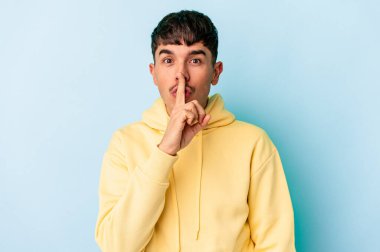 Genç melez adam mavi arka planda izole edilmiş bir şekilde sır saklıyor ya da sessizlik istiyor..