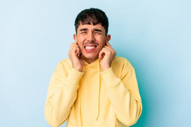 Genç melez adam mavi arka planda izole edilmiş kulakları elleriyle kapatıyor..