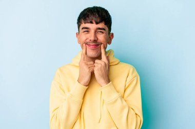 Genç melez adam mavi arka planda izole edildi. İki seçenek arasında şüpheye düştü..