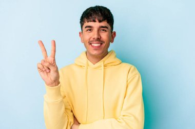 Genç melez adam mavi arka planda izole edilmiş. İki numarayı parmaklarıyla gösteriyor..