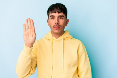 Genç melez adam mavi arka planda izole edilmiş gülümseyen beş numarayı parmaklarıyla gösteriyor..