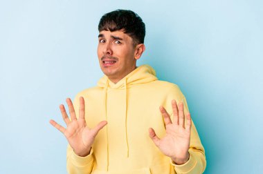 Genç melez adam, mavi arka planda izole edilmiş, tiksinti gösteren birini reddediyor..