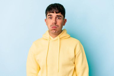 Mavi arka planda soyutlanmış genç melez adam yanakları patlatıyor, yorgun bir ifadesi var. Yüz ifadesi kavramı.